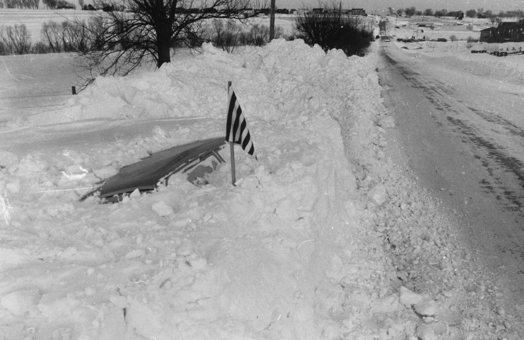 A striped flag warns snowplows of this buried car on Pacific Street.